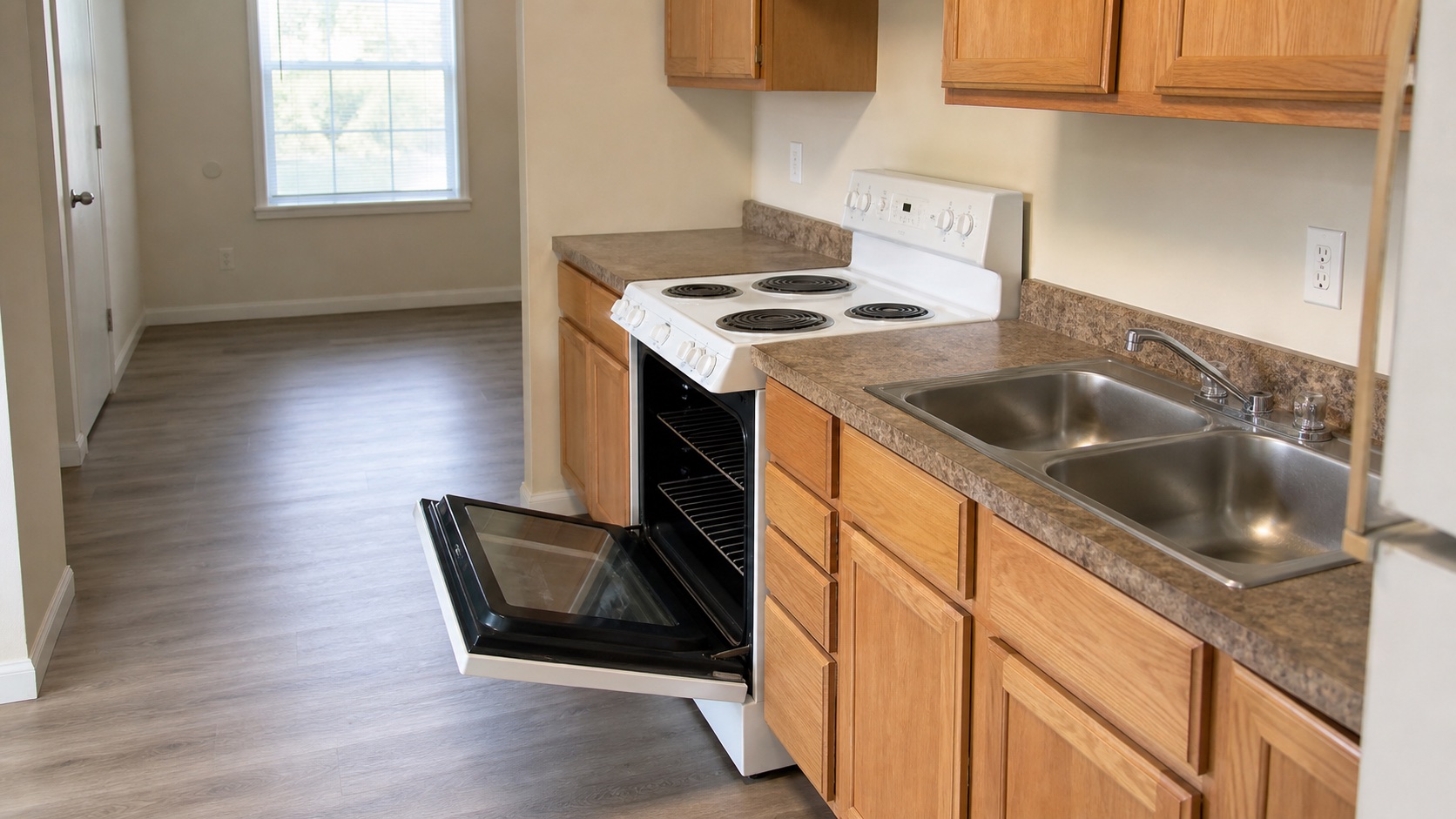 Empty rental kitchen with visible stovetop, sink, counters, and open oven after move-out cleaning.